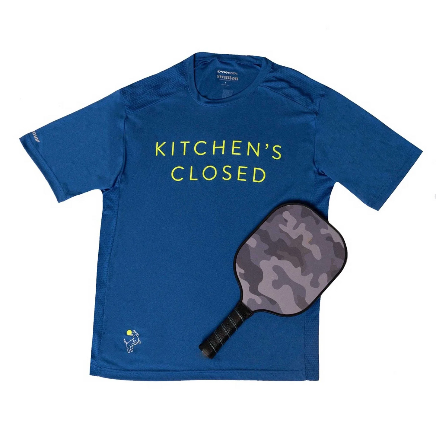 The Swinton Pickleball Men's Kitchen's Closed Performance Shirt in royal blue features “KITCHEN’S CLOSED” in yellow, shown with a gray camo pickleball paddle. Both are displayed on a white background.