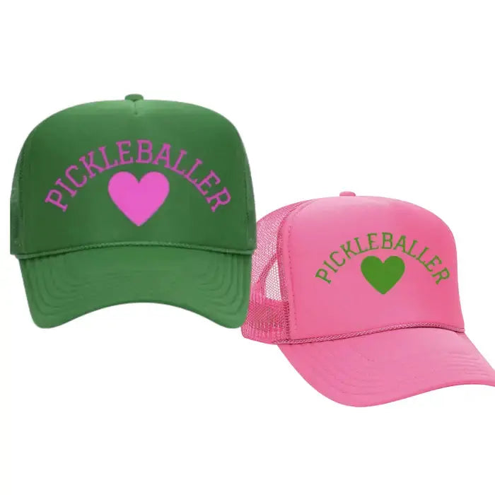 The Runway Athletics Pickleballer Trucker Hat is available in bold green or pink, each featuring "PICKLEBALLER" above a matching heart. These sporty mesh-back hats offer curved brims and vibrant style for pickleball fans.