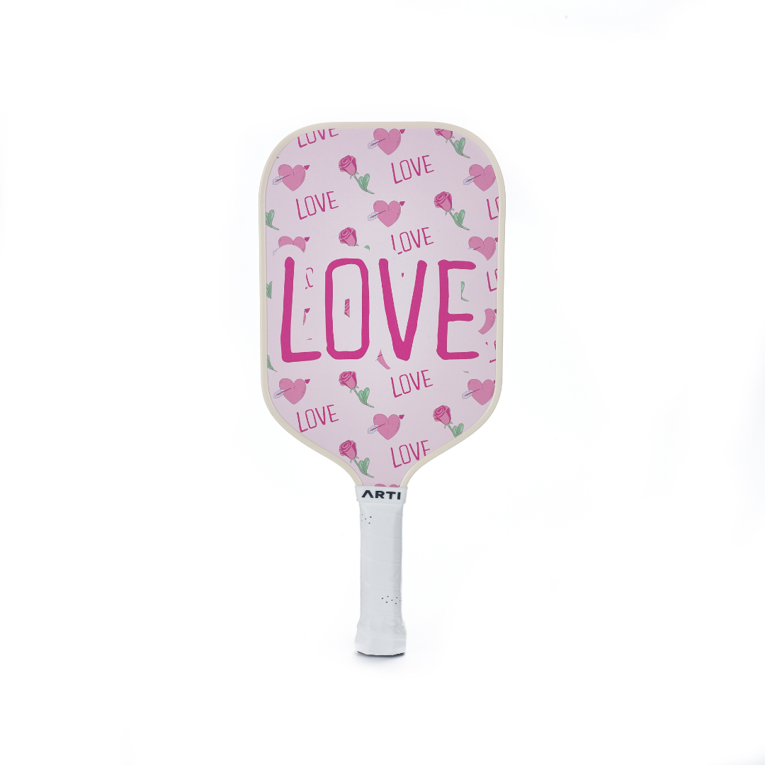 The ARTI Fiberglass "Valentine's" Pickleball Paddle Set by ARTI features a pink paddle with bold LOVE lettering, heart and rose designs, and a white-wrapped handle. Perfect for gifting or your collection. Shown on plain white background.