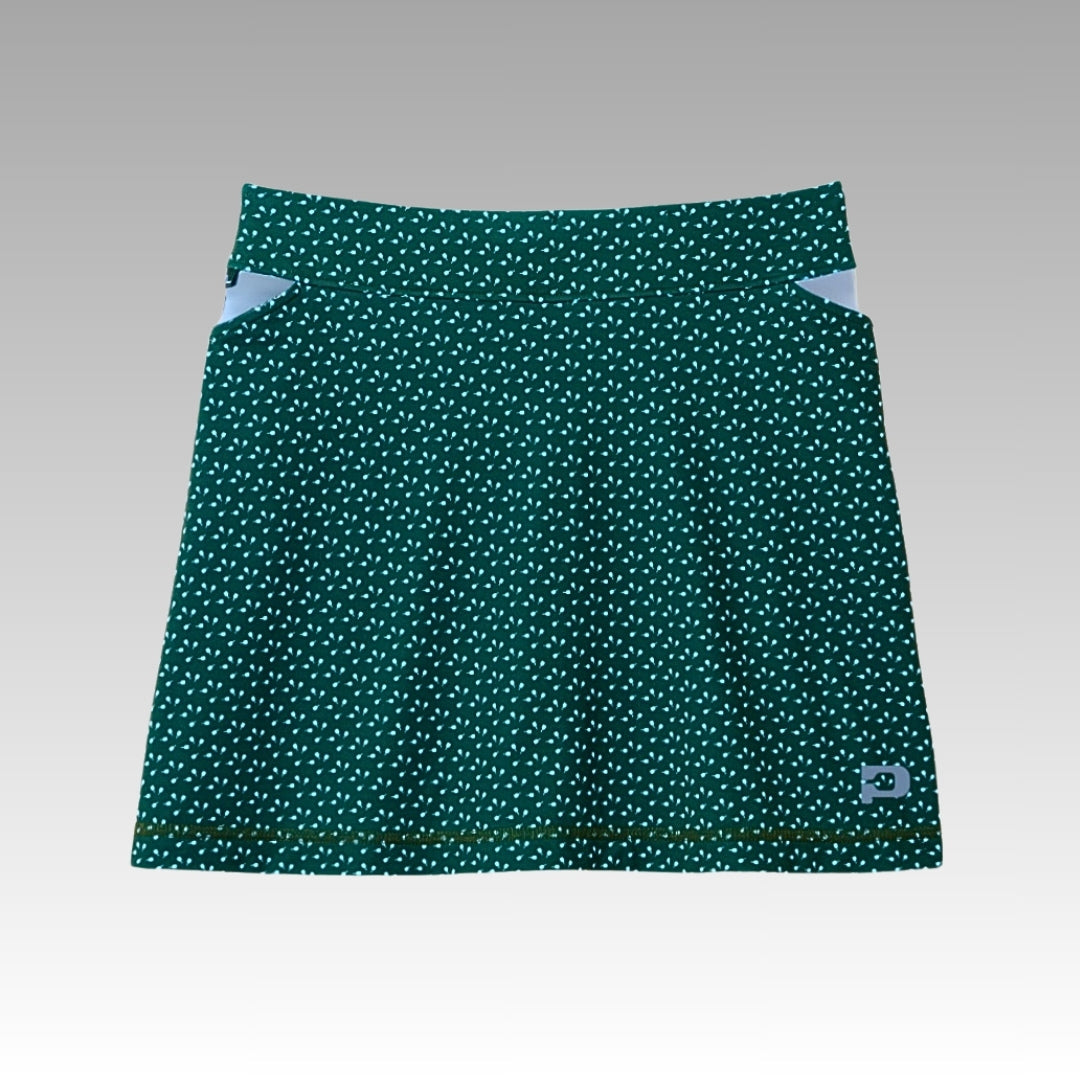The Playly Store Sammy Skort 2.0 is a green A-line pickleball skort with white dots, light blue waistband accents, and a hem logo patch. Made from CoolFlow fabric, it features a gray-to-white faded backdrop.