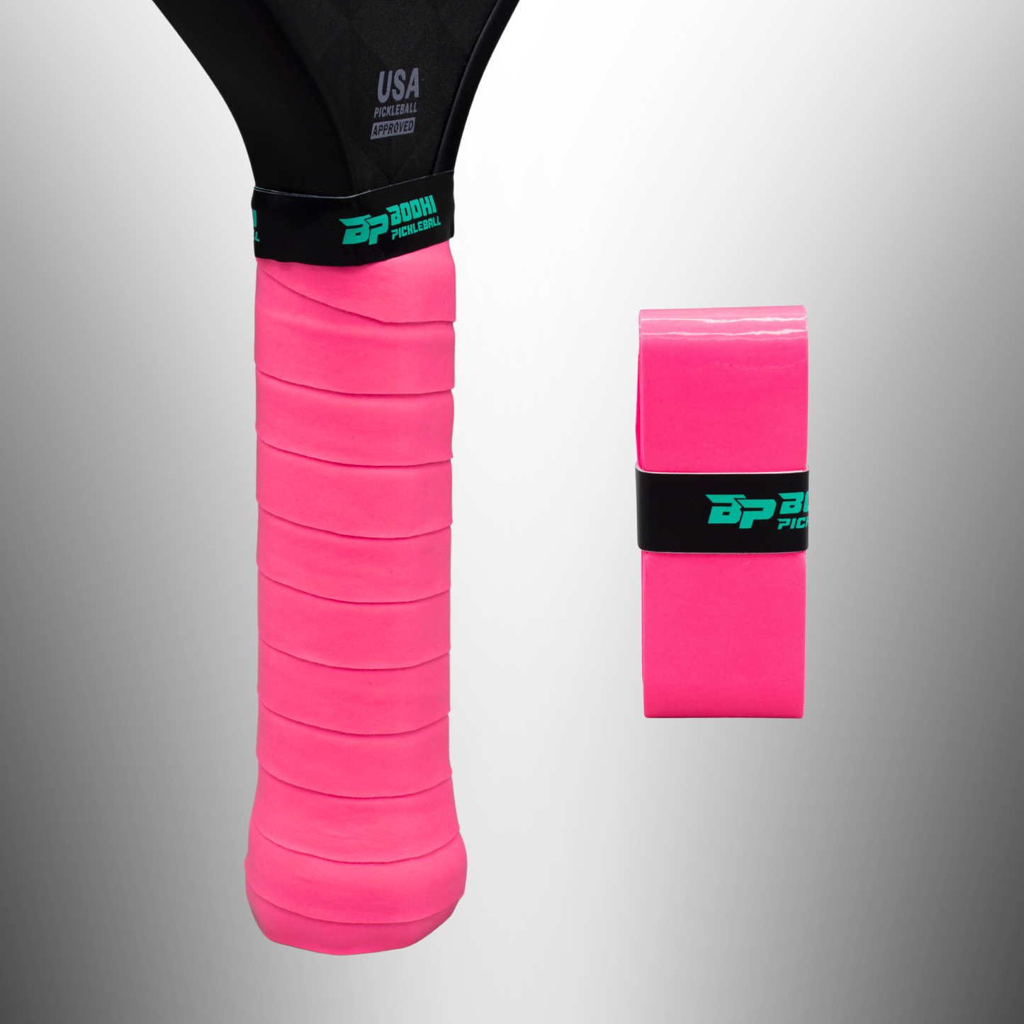 A close-up of a black pickleball paddle wrapped with a bright pink PROtack™ Premium Pickleball Overgrip by Bodhi Performance. An unused overgrip, secured with a black and teal “BP” band, rests nearby on a gradient gray background.