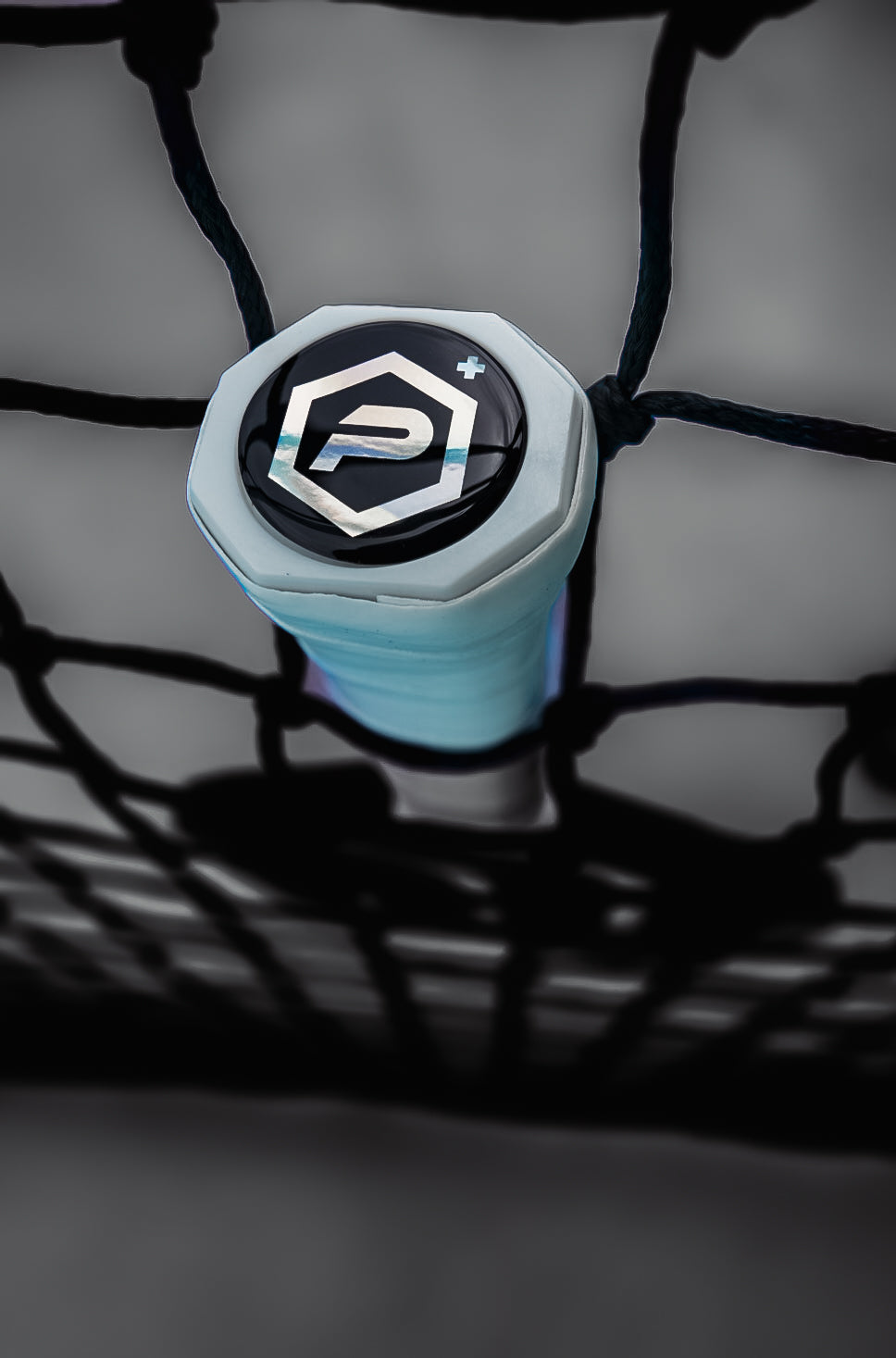 Close-up of Potenza Pickleball's Carbon Nanotubes+ COREx3 paddle handle in light blue with a black and silver P+ logo, showcasing COREx3 technology and textured grip as it rests against a black sports net.
