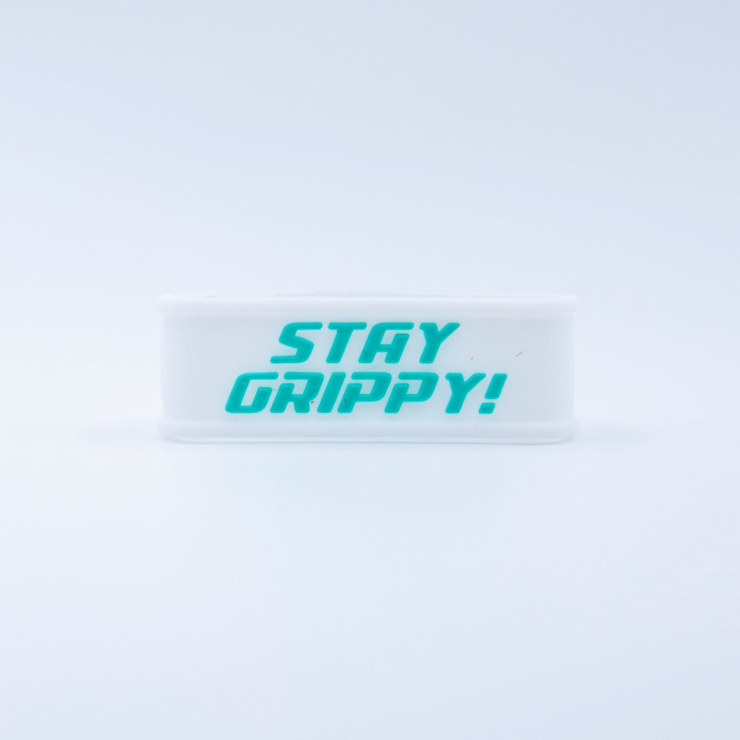 A white Bodhi Performance Paddle Band with bold turquoise "STAY GRIPPY!" text stands upright on a plain background—one of the essential pickleball paddle accessories, combining clear style and function.