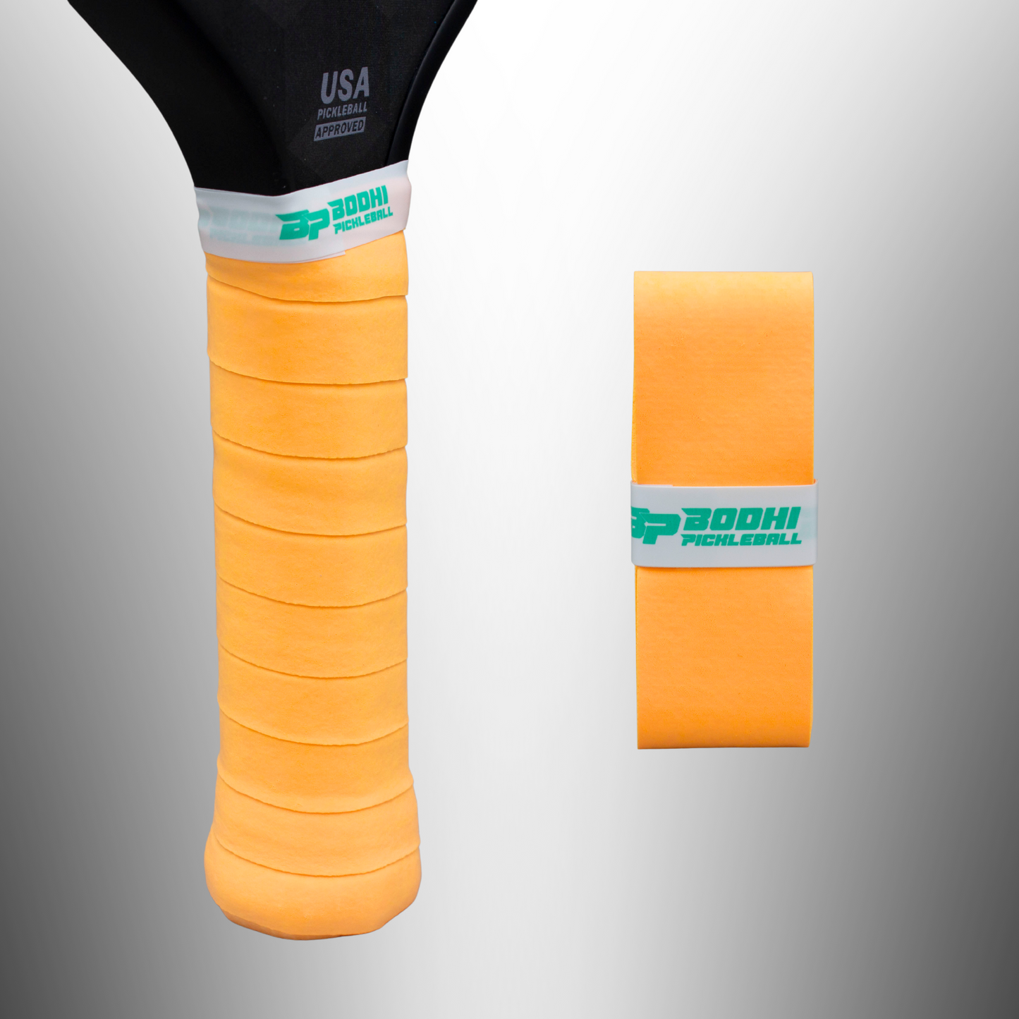 An orange Bodhi Performance DRYtack™ Premium Pickleball Overgrip is wrapped around a paddle handle, with a matching replacement beside it. Both grips feature “BODHI PICKLEBALL” in green and offer excellent moisture control.