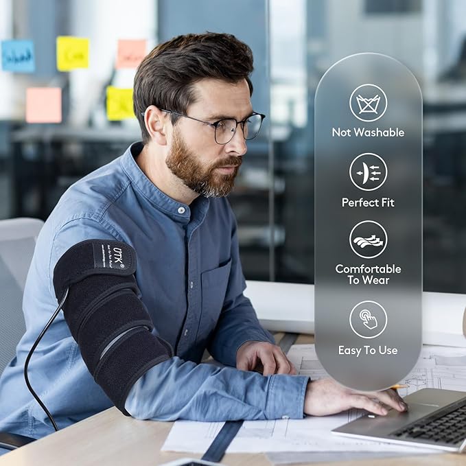 A bearded man with glasses wears the iReliev Far Infrared Heating Pad Wrap with Far Jade at his desk, working on a laptop amid documents. Overlay: Not Washable, Perfect Fit, Comfortable to Wear, Easy To Use.