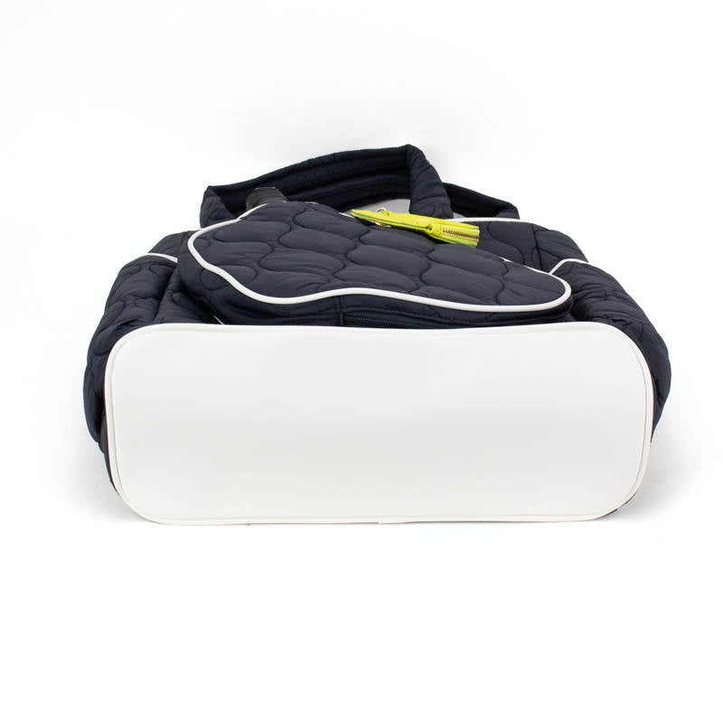 A large black quilted Fifth Ave Pickleball Convertible Tote Bag/Backpack by Queen of the Court lies on its side with a white base facing the camera, topped with a matching accessory and yellow item, all on a white background.