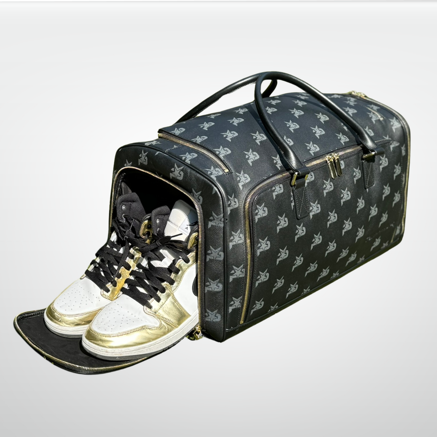 The iReliev I AM - Leather Monogram Training Duffel Bag in black features a white butterfly pattern and is open at one end, showing stylish high-top sneakers in white, black, and metallic gold against a plain light gray background.