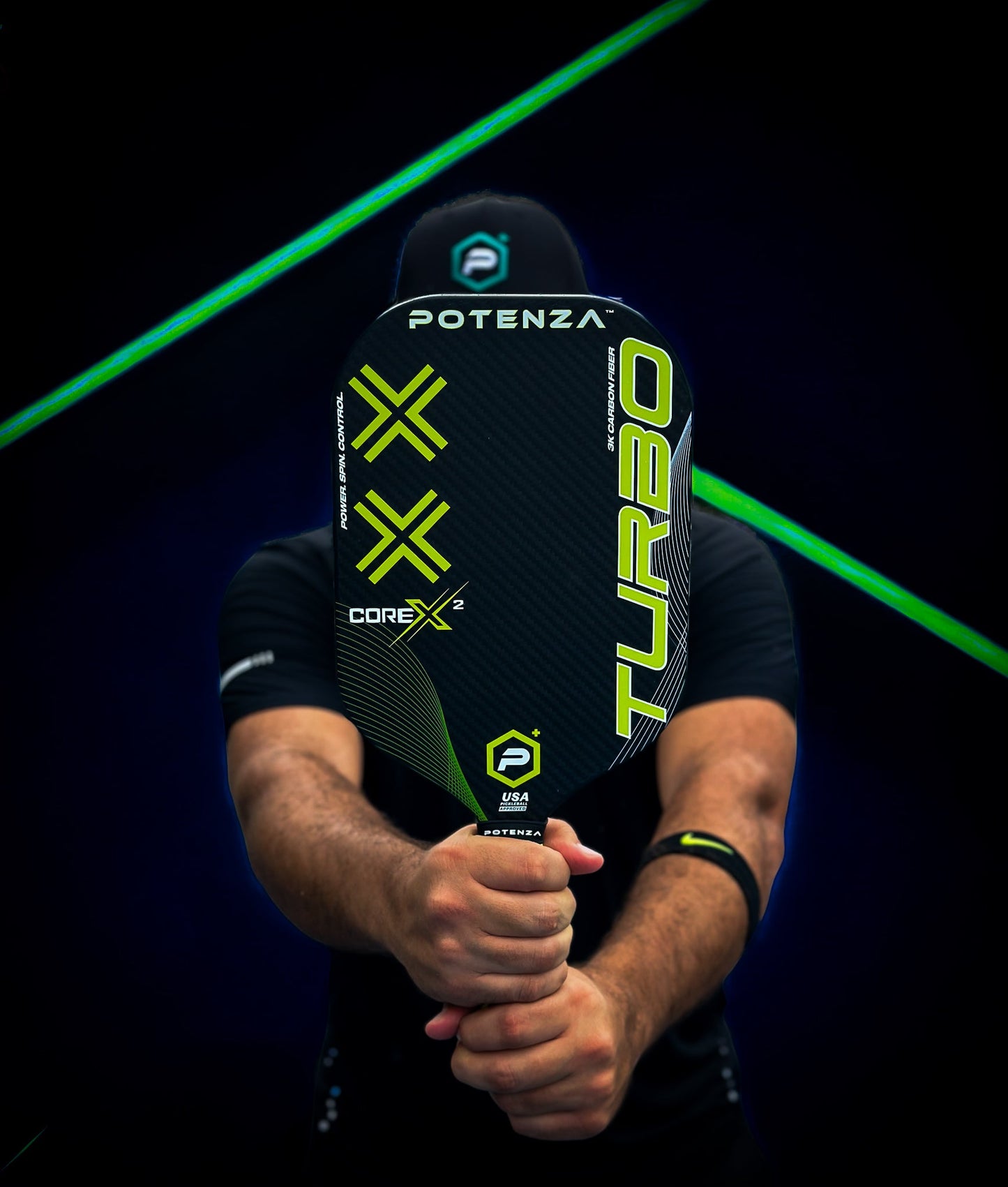 A person holds a Potenza Pickleball TURBO+ COREx2 paddle, featuring “COREx2” branding, in front of their face. Neon green lines light up the dark backdrop, matching neon accents on their black shirt and cap.