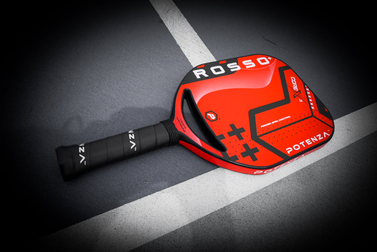 A red and black Potenza Pickleball ROSSO+ COREx3 paddle lies diagonally on a dark court across a white line. The 21mm paddle has a textured handle wrapped in black grip tape displaying “POTENZA.”.