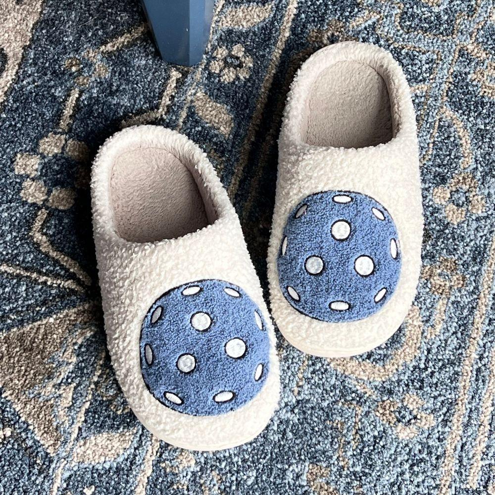 Fresh Pickle's Pickleball Slippers—fluffy white and cozy with textured blue circles and white dots—feature open backs and rest on a blue patterned rug with floral and geometric designs.