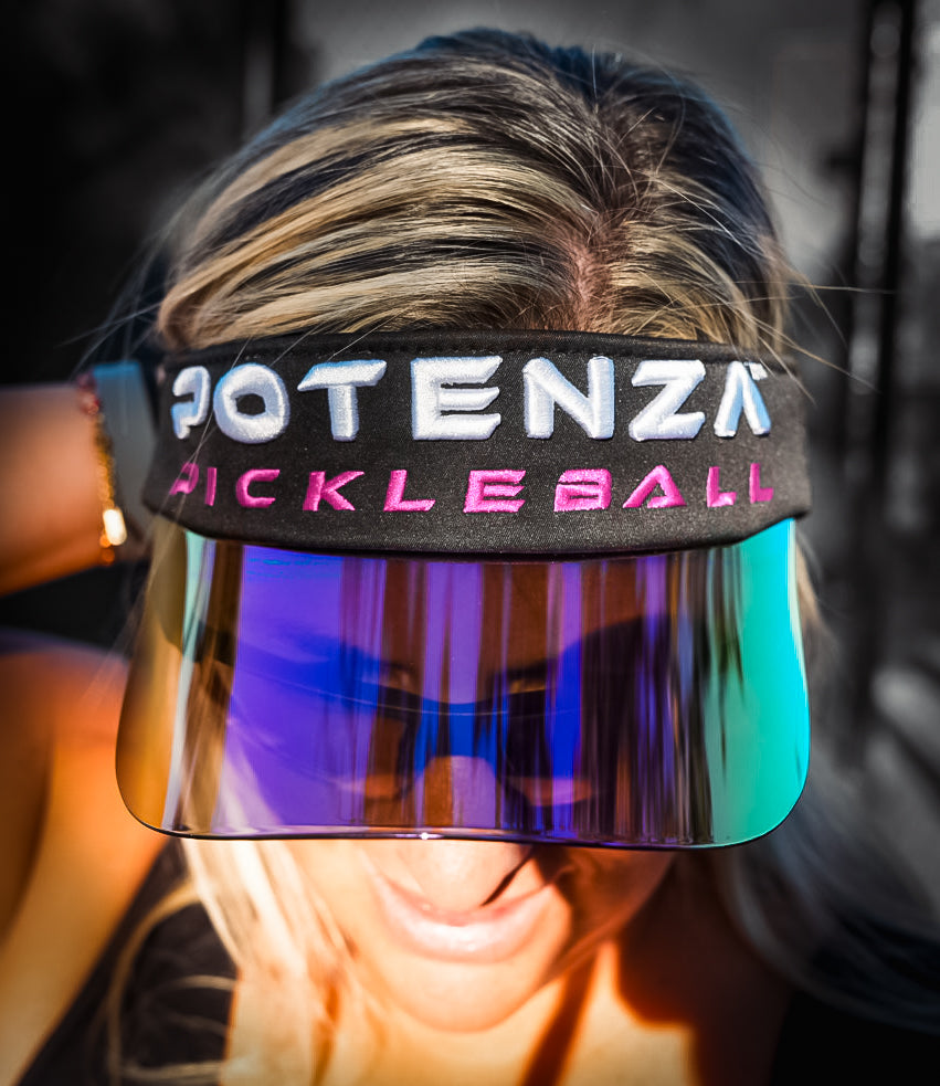 A blonde woman wears the Potenza Pickleball Performance Solar Visor with a holographic brim and “POTENZA PICKLEBALL” in white and pink, standing out against a grayscale background.