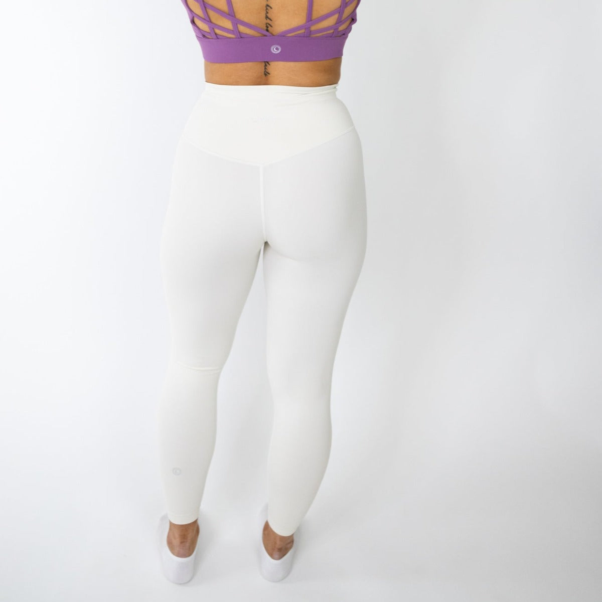 A person faces away from the camera, showcasing DYM Athletics' Seamlessly Free Legging | SALE in buttery soft fabric. Only the lower half and part of the back are visible against a plain white background.