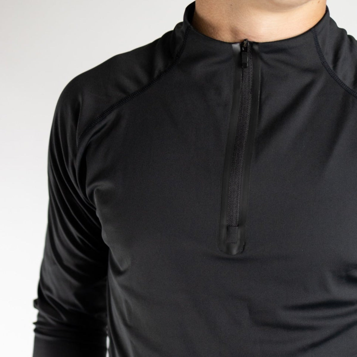 A man models the Top-Notch Men's 1/4 Zip by DYM Athletics, a fitted black long-sleeve athletic shirt with high collar and short front zipper, quick-drying and smooth textured, shown against a plain white background.
