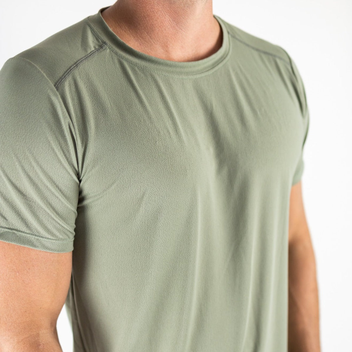 A man wears the Elevate Men's Lightweight Breathable Tee by DYM Athletics in light olive green, featuring subtle shoulder stitching and mesh panels for comfort—ideal for casual wear or running. Now on SALE.