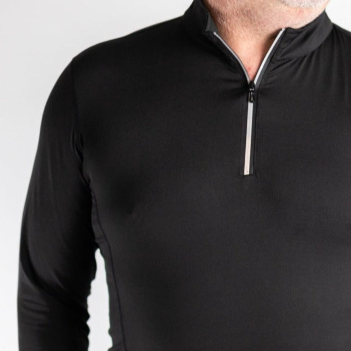 A close-up shows a person wearing the DYM Athletics FLEX Men's 1/4 Zip—black, fitted, with a short front zipper—revealing only the lower face, neck, chest, and upper arms against a plain white background.