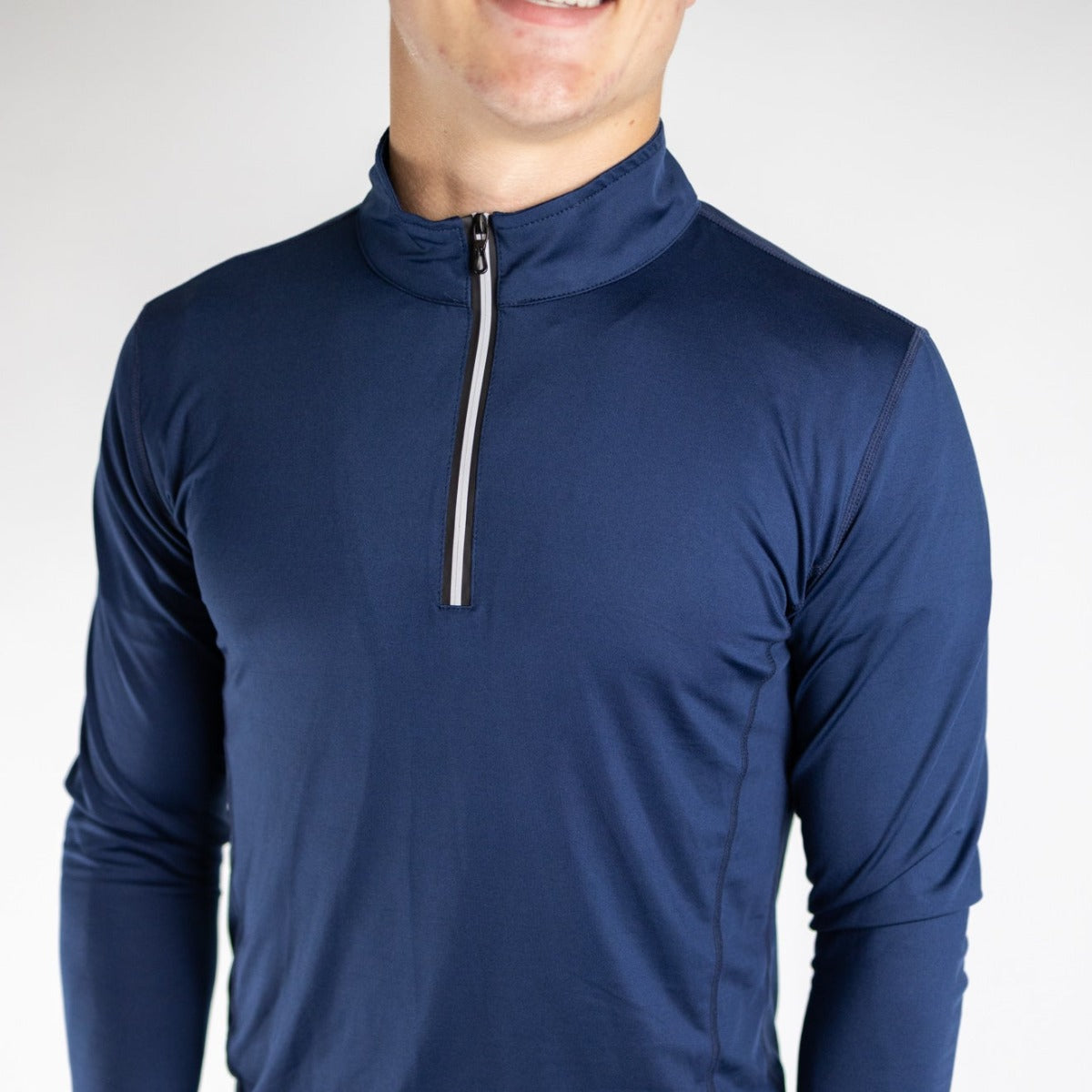 A person wears the DYM Athletics FLEX Men's 1/4 Zip—a navy long-sleeved, quick-drying pullover—standing against a plain white background, with only their upper body and lower face (smiling slightly) visible.