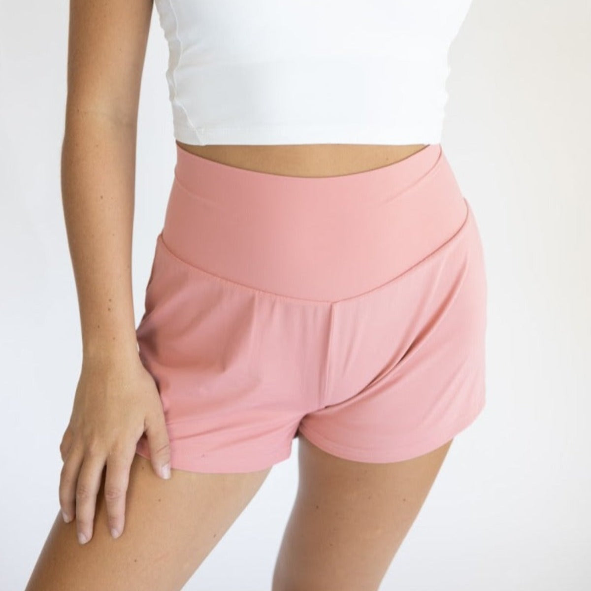 A person models DYM Athletics’ Namaste Yoga Shorts | 3", featuring a smooth, high-rise waistband and soft fabric. They pair it with a white crop top, standing against a plain white background with one arm relaxed by their side. Only the torso and upper legs are visible.