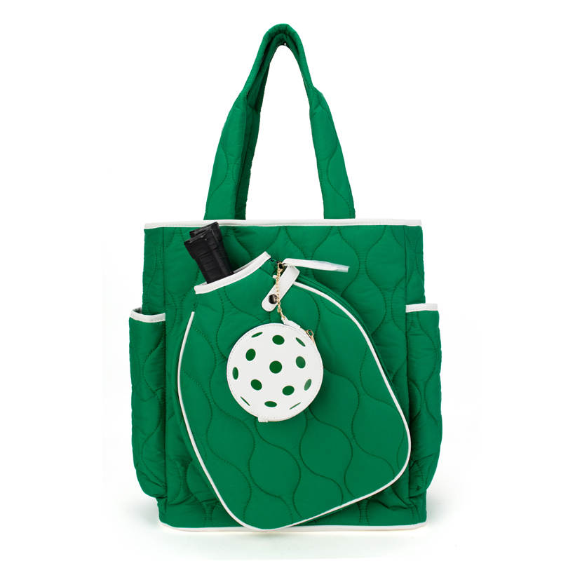 The Queen of the Court Fifth Ave Pickleball Convertible Tote Bag/Backpack is green with white trim, two handles, side pockets, a white ball with green holes attached to the front, and a partially visible black-handled paddle inside.