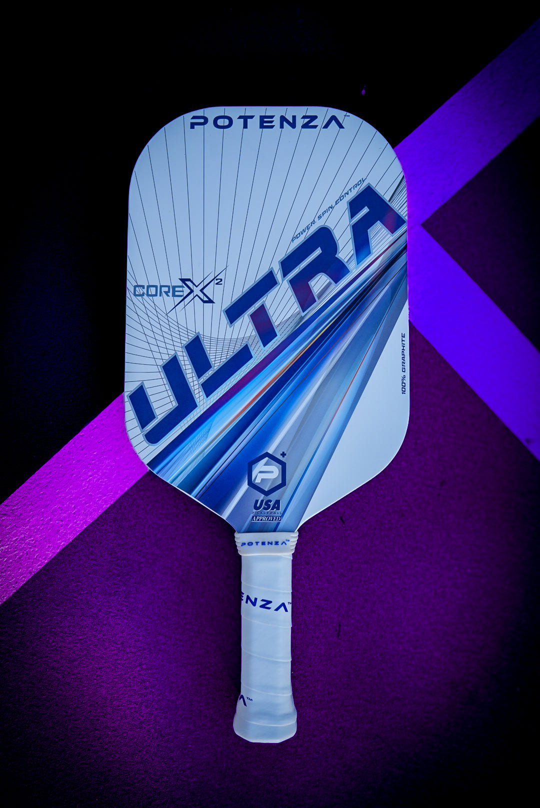 The Potenza Pickleball ULTRA+ COREx2 paddle, featuring a white edgeless design with bold blue and gray graphics and a white grip handle, rests on a purple surface crossed by a diagonal magenta stripe.