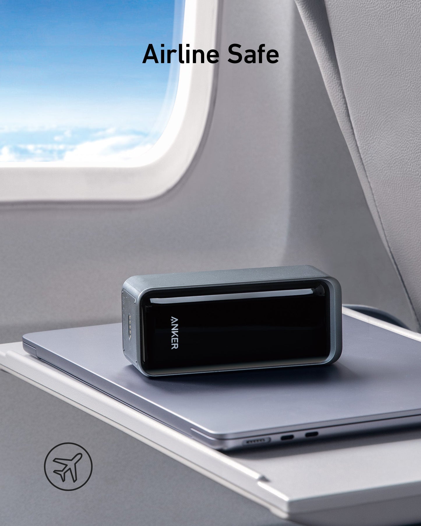 An Anker Prime Power Bank (20K, 200W) by Anker sits on a silver laptop on an airplane tray table beside a window, with sky and clouds outside. "Airline Safe" text appears above, and a small airplane icon is in the bottom left corner.