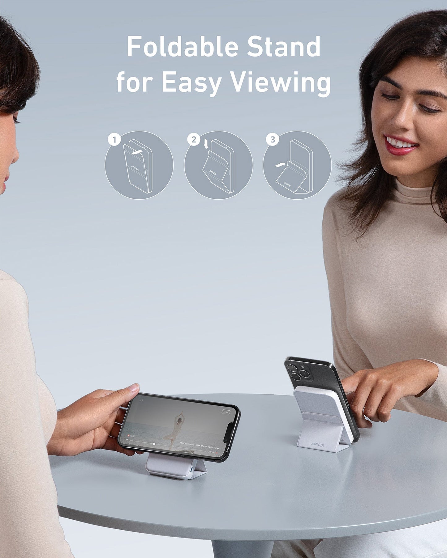 Two women sit at a round table, each using the Anker 622 Magnetic Battery (MagGo) as a foldable stand for their phones. Instructional icons show how to fold the stand. Text reads: Foldable Stand for Easy Viewing. Both appear engaged and relaxed.