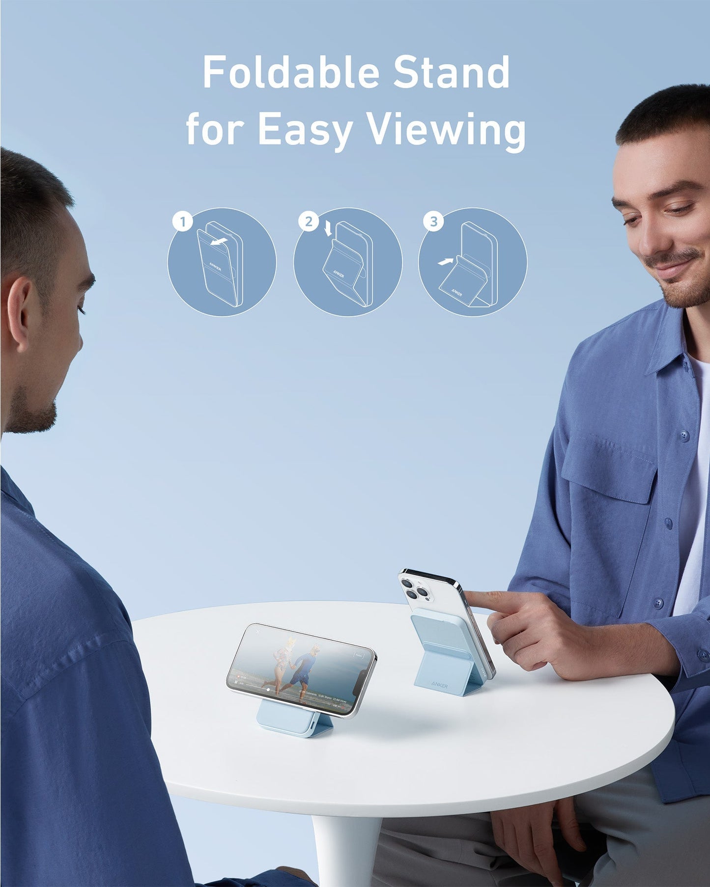 Two men sit at a round white table. One uses an iPhone with the Anker 622 Magnetic Battery (MagGo) by Anker as a foldable stand, while the other holds his phone. Text above reads Foldable Stand for Easy Viewing with setup steps on light blue.