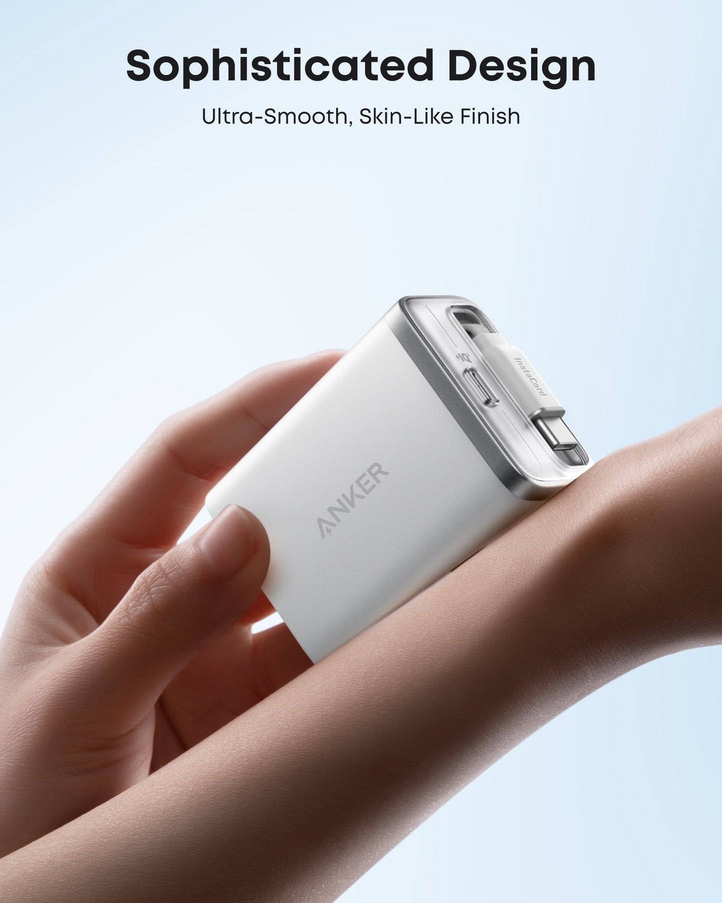 A hand holds a compact, silver Anker Nano Charger (35W) with a built-in retractable USB-C cable. Soft lighting shows off its pocket-friendly, ultra-smooth, skin-like finish. “Sophisticated Design – Ultra-Smooth Feel” appears on a light blue background.