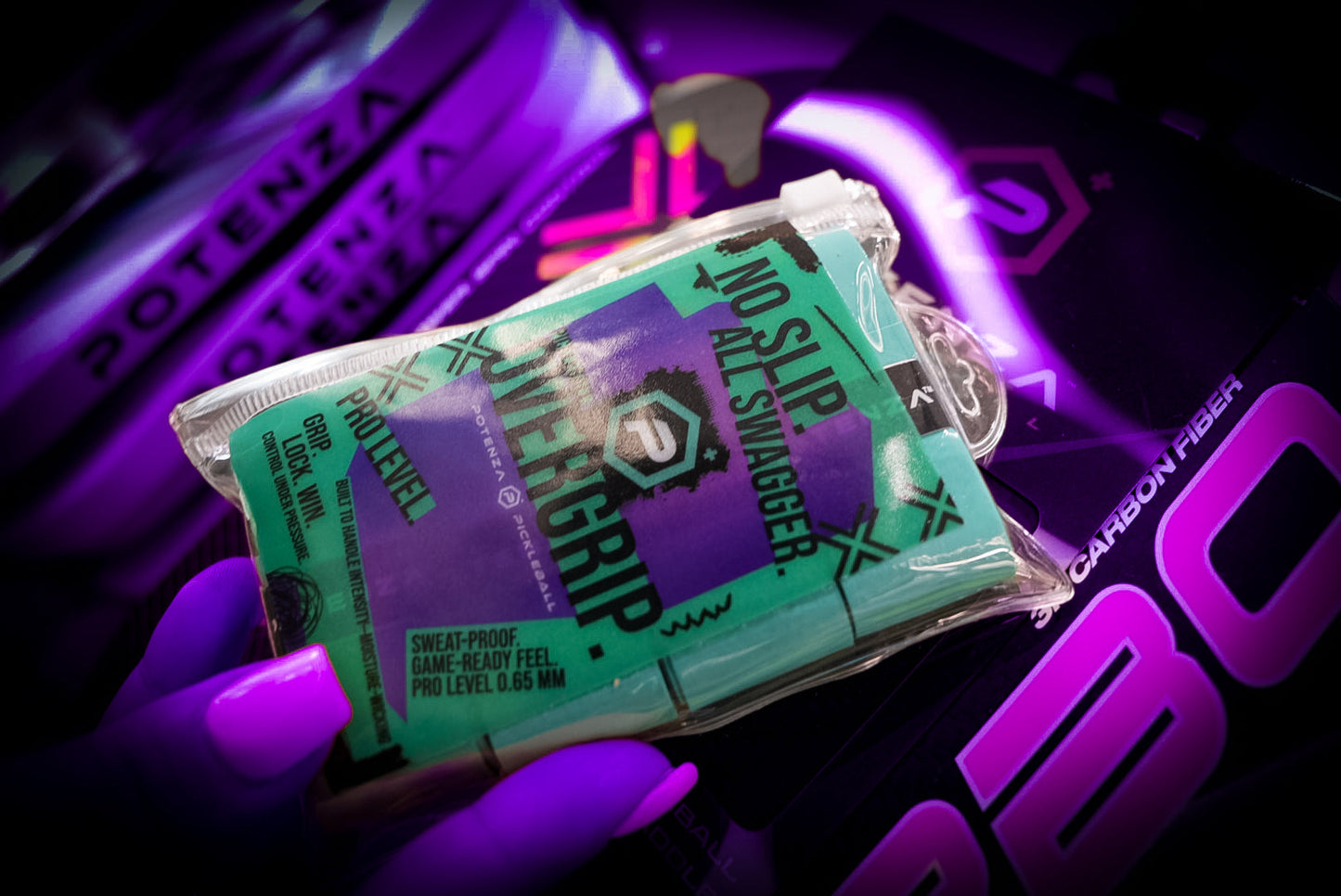 A close-up of a hand with purple-painted nails holding a teal Potenza Pickleball PROX Tacky Overgrip (4-pack) labeled "NO SLIP. ALL SWAGGER." with other Potenza sports gear and purple lighting in the background.