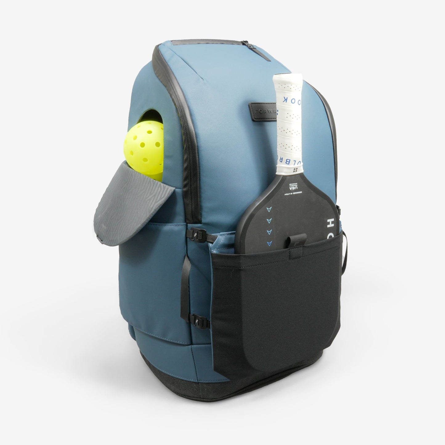 The FORWRD Court Caddy Front Paddle Sleeve is a blue backpack with black zippers and straps, offering a front sleeve for your paddle and a side pocket for a yellow perforated ball. Features are clearly visible against the white background.