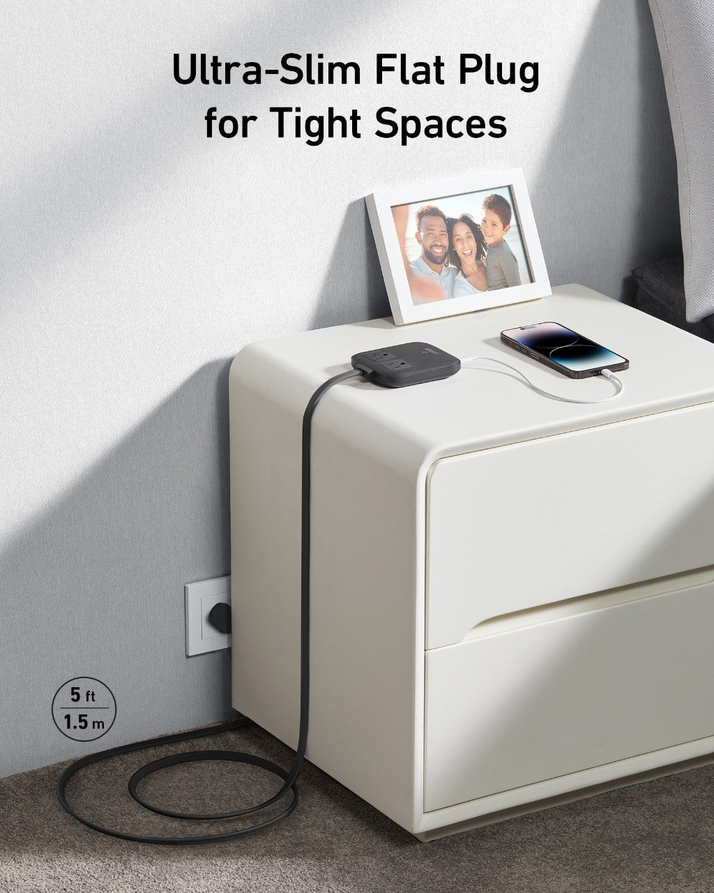 An Anker Nano Charging Station (6-in-1, 67W) in black with USB-C charging is plugged into a wall and rests on a white nightstand near a smartphone and framed photo. Text reads: Ultra-Slim Flat Plug for Tight Spaces, 5 ft | 1.5 m cord length.