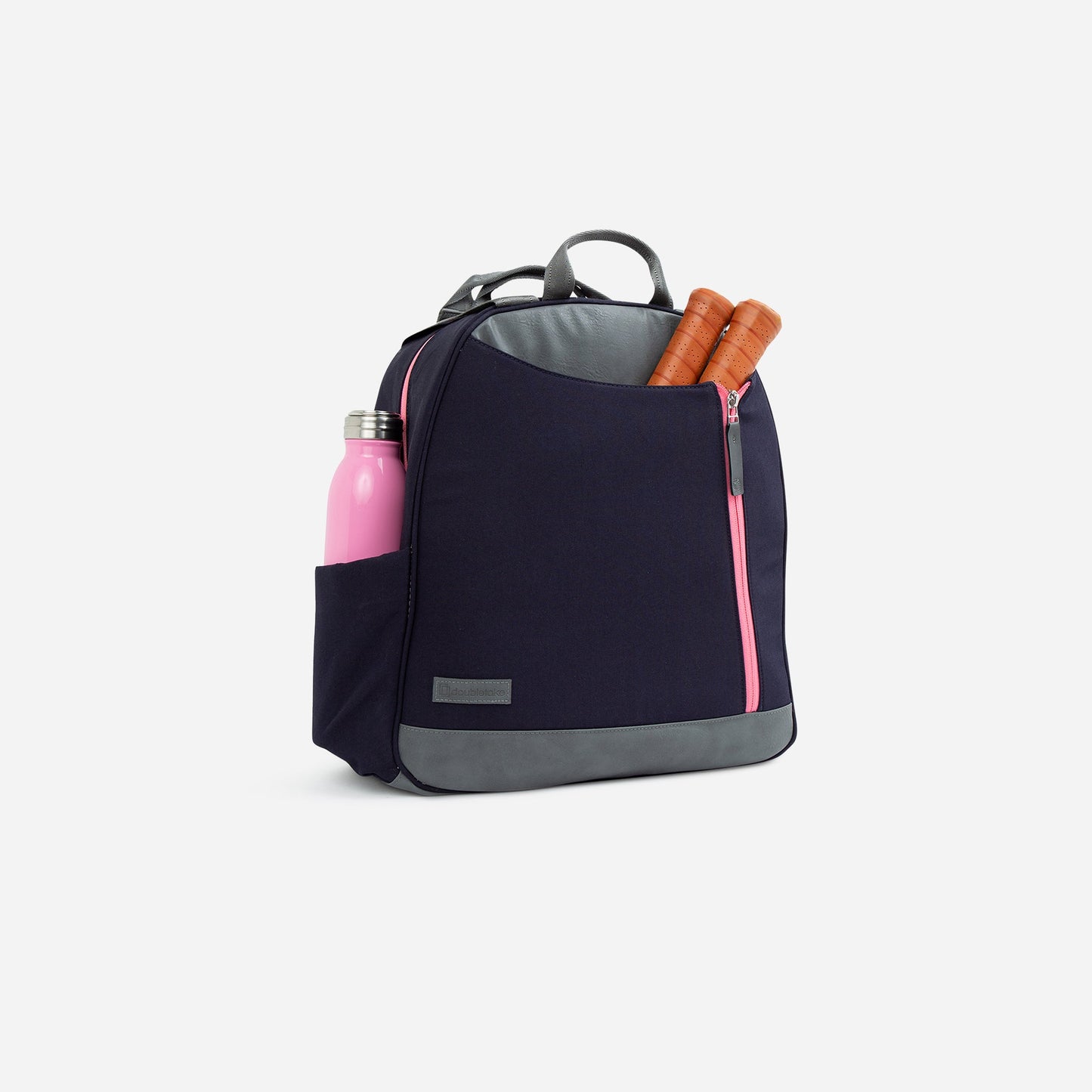 The Doubletake MELBOURNE Pickleball Backpack & Tote, in navy blue and gray with pink zipper and handle, is water-resistant. Shown against a white background, its side pocket holds a pink water bottle; the front pocket has two baguettes.