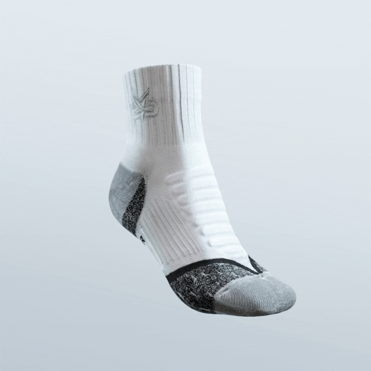 An iReliev AMP Ankle Compression Sock floats against a light gray background. Mostly white, it features textured ankle ribbing, a gray reinforced heel and toe, black arch accents, and a subtle logo near the top.