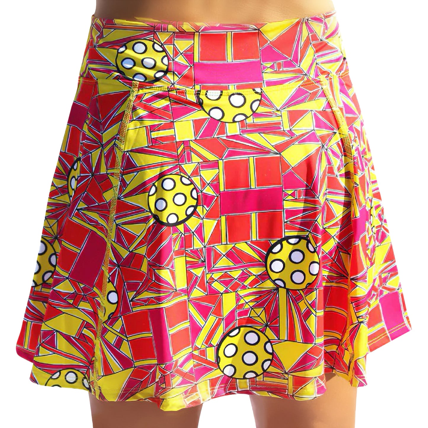 The Pickleball Bella PB Aline Skort Angle Shot 1 is a flared skort with a bold geometric pattern in red, yellow, and pink with black outlines and polka-dotted circles. Shown waist to mid-thigh, it offers UV protection for active play.