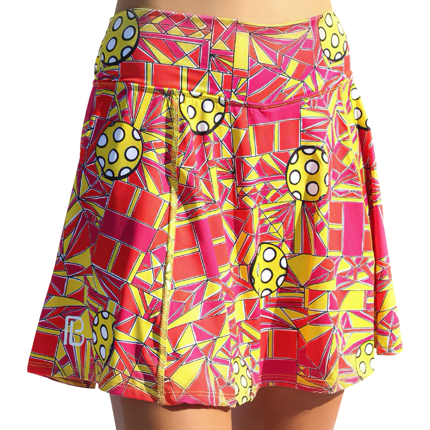 The Pickleball Bella PB Aline Skort Angle Shot 1 features a vibrant geometric pattern in red, pink, and yellow with yellow circles, white dots, pleats, UV protection, and moisture wicking for active comfort.