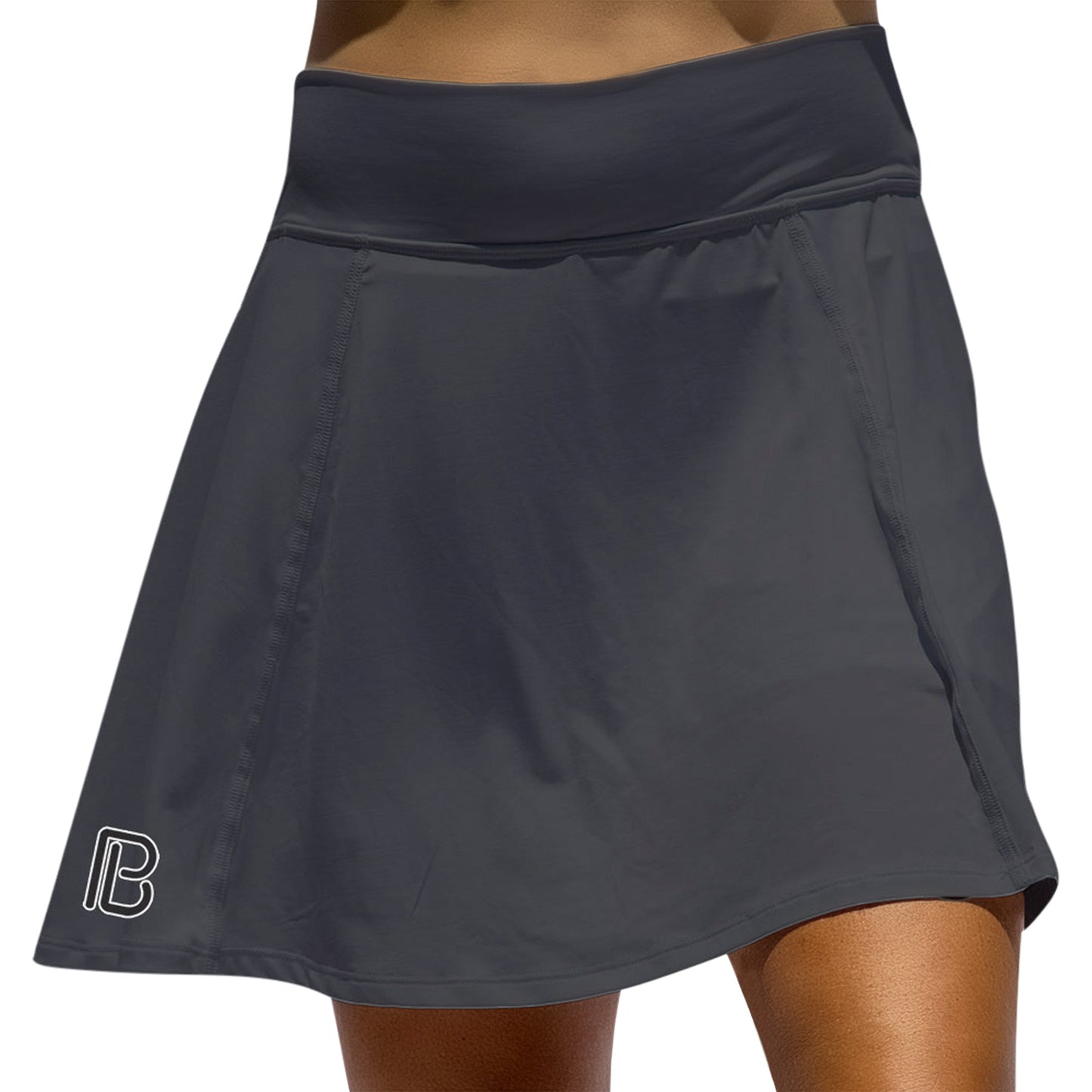 A close-up of a person wearing the Pickleball Bella PB Aline Skort Black, featuring a wide waistband and a white “PB” logo near the left hem. The smooth, stretchy fabric is highlighted, making it ideal court attire.