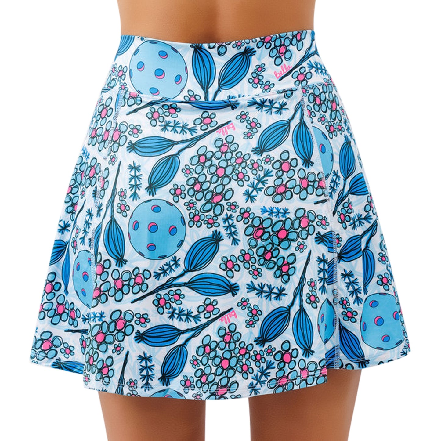 A woman wears Pickleball Bella's PB Aline Skort Bloomers, a short high-waisted skirt with 4-way stretch. Blue leaves, berry clusters, and pink-dotted shapes adorn the crisp white fabric in a whimsical botanical pattern.