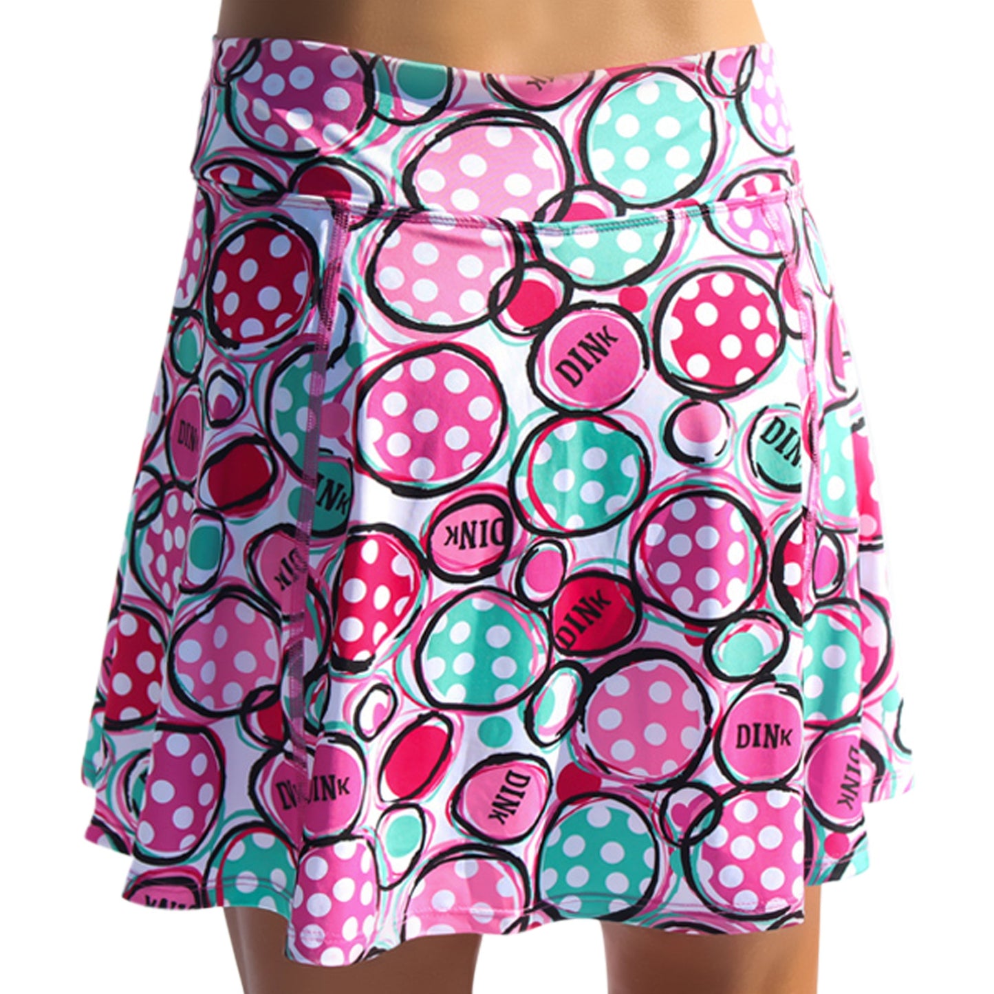 The Pickleball Bella PB Aline Skort Dink 2 is a vibrant pickleball skirt with playful pink, teal, and white polka dot circles—some featuring "DINK" in bold. Shown from the waist down on the wearer.
