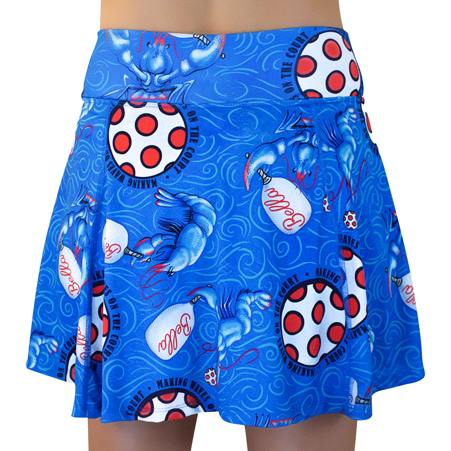 The Pickleball Bella PB Aline Skort Lobster Monster is a blue, flared pickleball skirt with bold blue dragons, white paddles with red dots, “pickle” in red script, swirling lines, and black text reading “MAKING WAVES ON THE COURT.”.