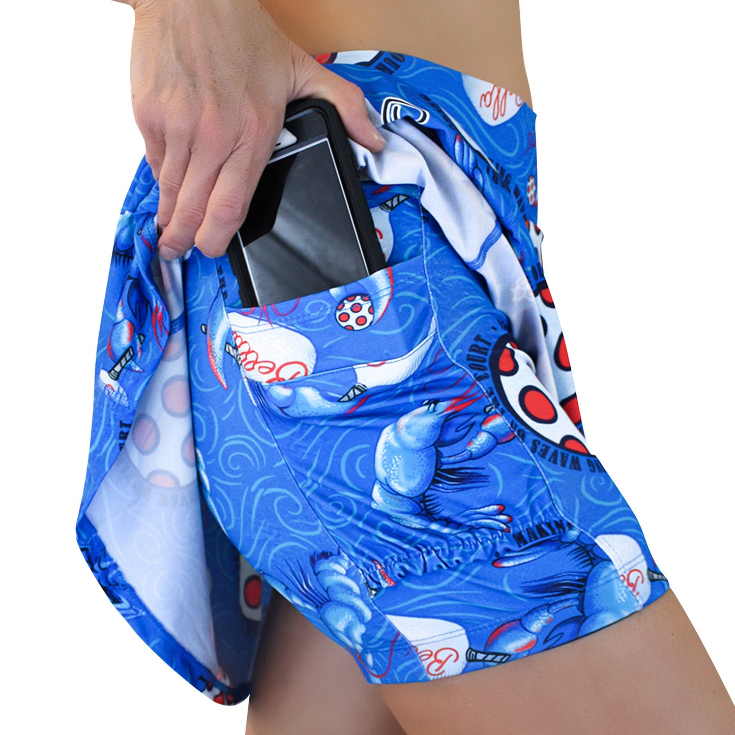 A person is slipping a smartphone into the side pocket of Pickleball Bella’s PB Aline Skort Lobster Monster, showcasing its playful lobster pattern and practical phone fit against a plain white background.
