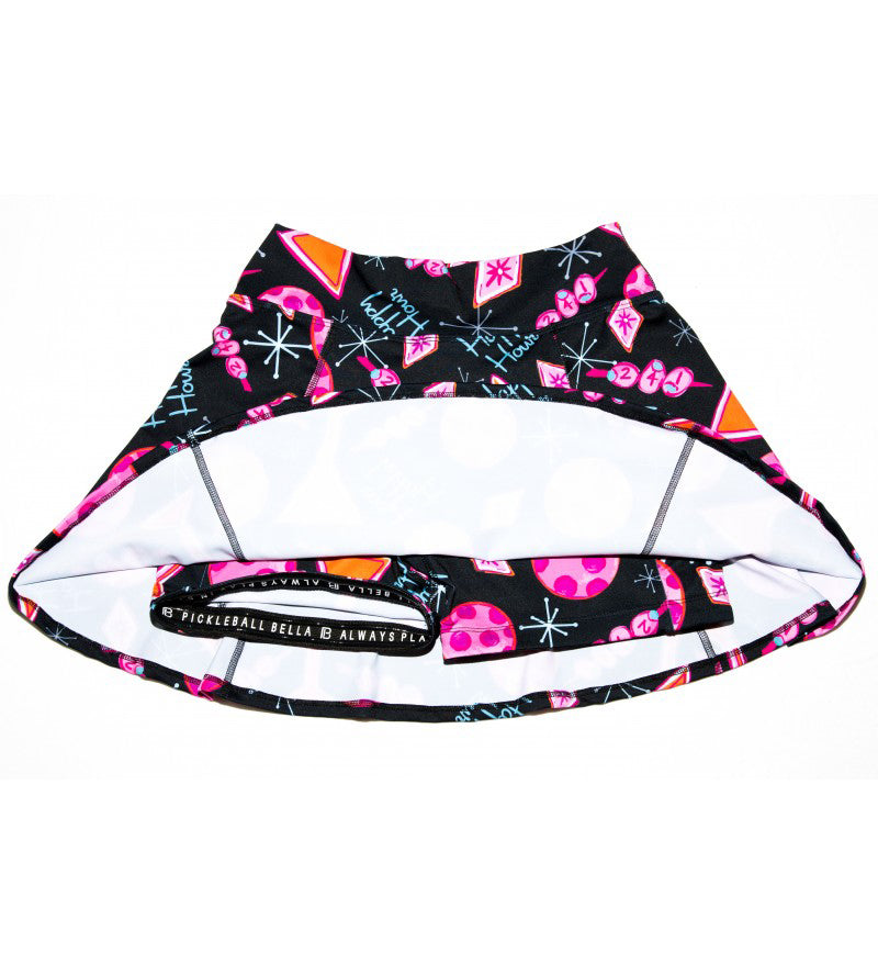 The Pickleball Bella PB Aline Skort Martini 2-4-1 Happy Hour is a flared, black athletic skirt with pink pickleball-themed prints, “PICKLEBALL BELLA ALWAYS PLAY” on the waistband, and a visible inner lining.