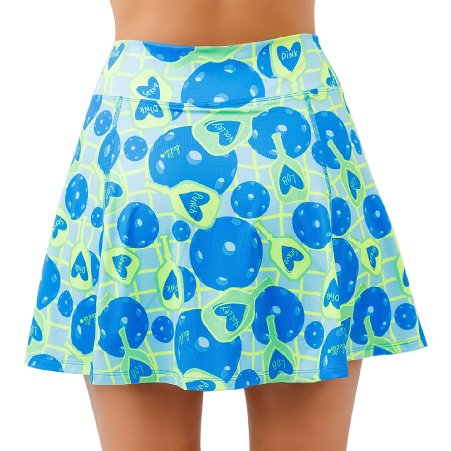 A person wears Pickleball Bella’s PB Aline Skort Net Worth, a high-waisted, flared athletic skirt featuring blue mushrooms and green hearts on a light grid background. The knee-length skort’s midsection and upper thighs are visible.