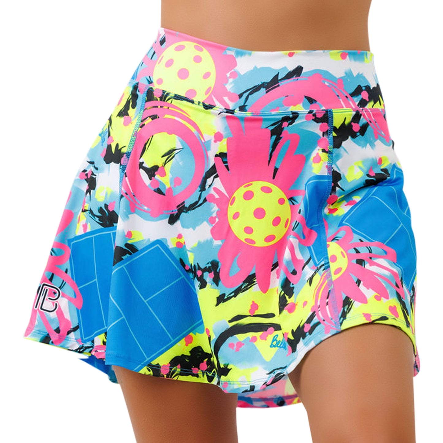 A close-up of the Pickleball Bella PB Aline Skort Open Play, an athletic A-line skirt with a vibrant abstract pattern in pink, yellow, blue, and black. Featuring large polka dots, paint splatters, a wide waistband for comfort, and built-in compression shorts.