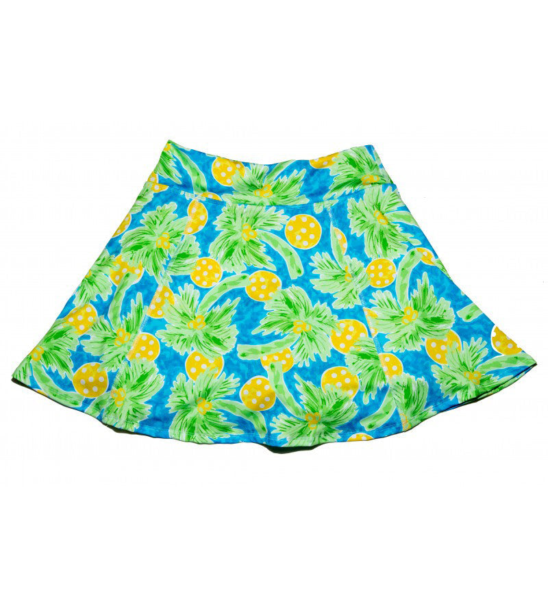 The Pickleball Bella PB Aline Skort Palms 1 is a flared, A-line pickleball skort featuring a wide waistband and a vibrant print of green palm leaves and yellow pineapples on a blue background, shown laid flat against white.