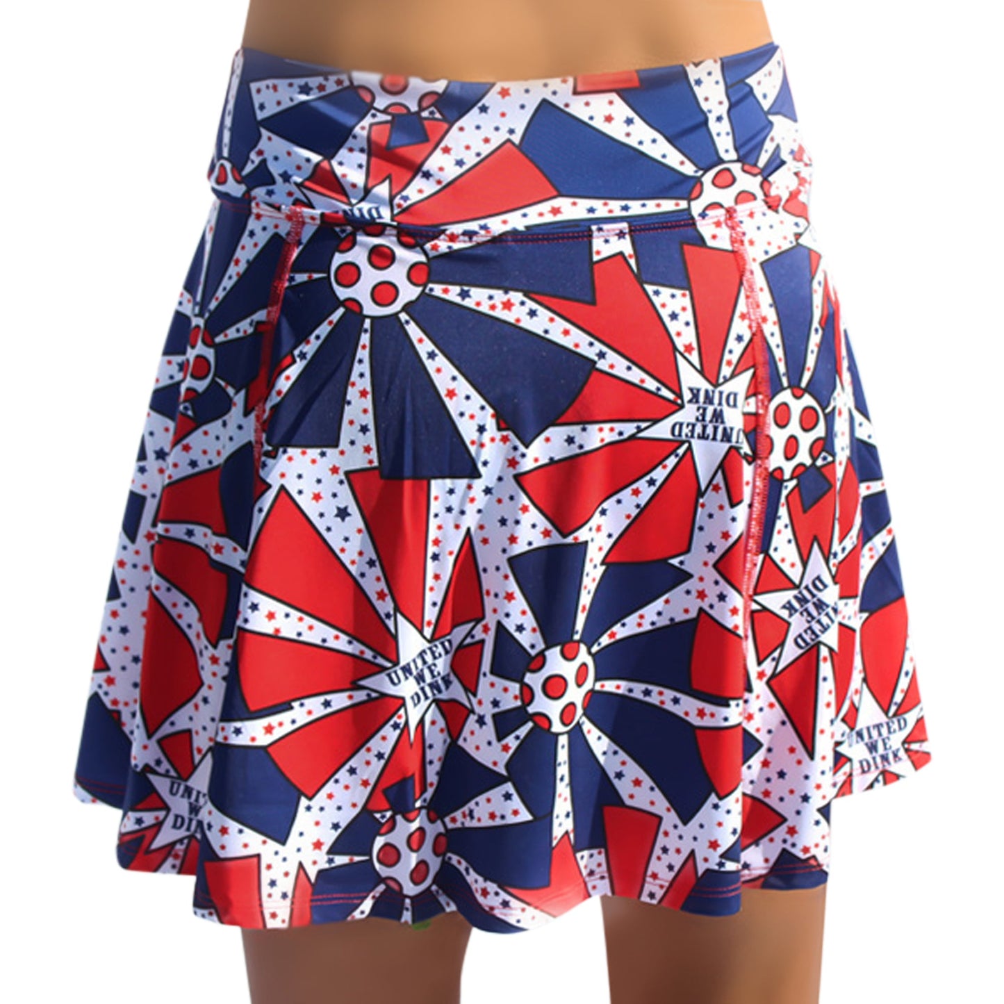 The Pickleball Bella PB Aline Skort United We Dink features a flared, pleated design with bold red, white, and blue starbursts, polka dots, and “UNITED WE DINK” text—a standout patriotic pickleball skort.