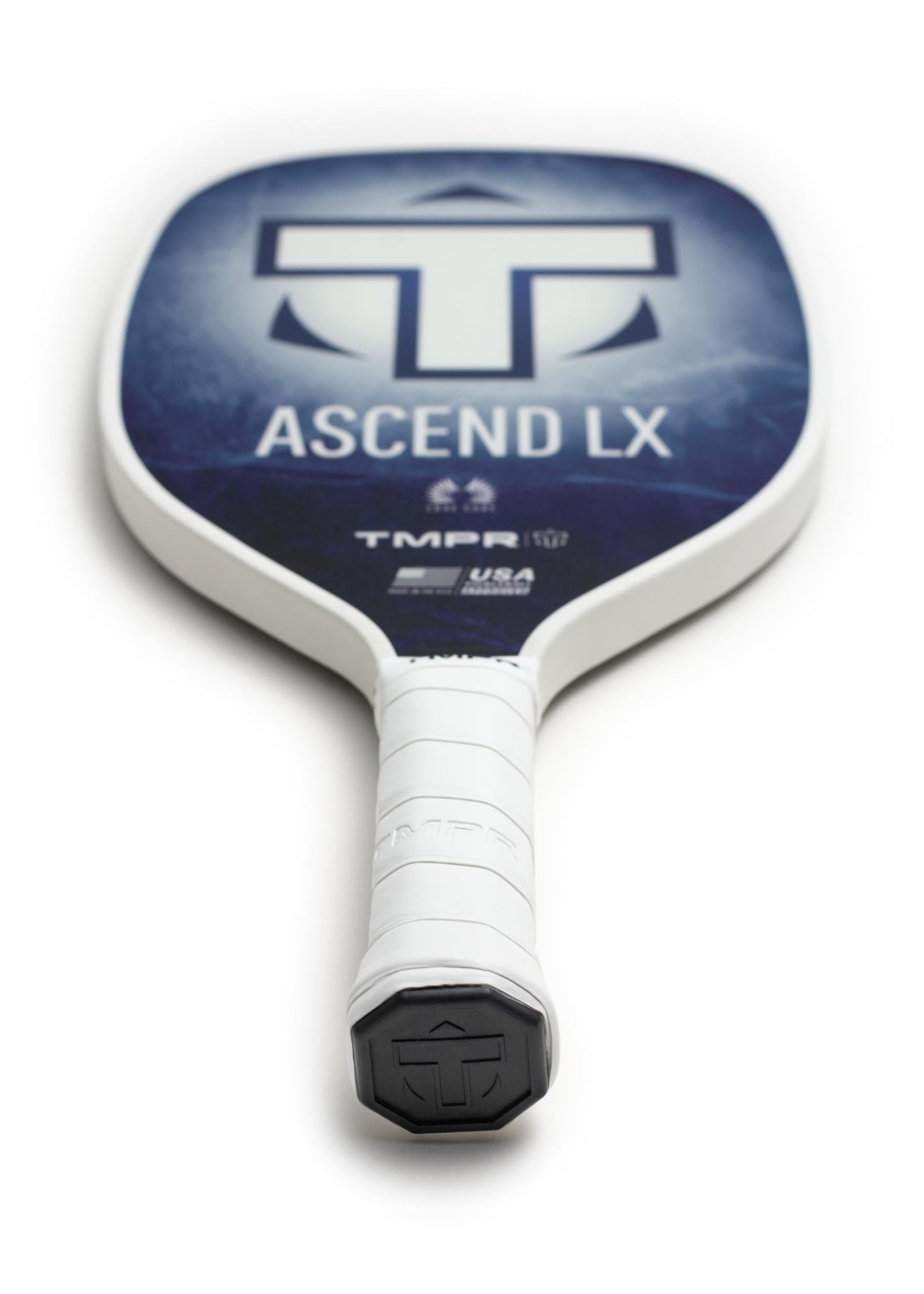 A close-up image shows the TMPR Sports Ascend LX | Indigo Ice pickleball paddle, featuring a long handle with white grip tape, a black end cap, and a blue face displaying the “TMPR” logo. The paddle rests on a white surface.