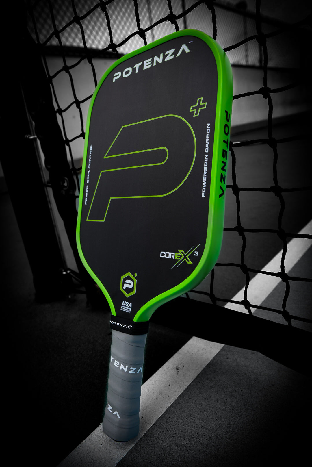 A Potenza Pickleball P+ PowerSpin Carbon COREx3 paddle (Neon Green, Elongated Face) with a large P logo, “Potenza+” and “COREx3” branding, plus a grey overgrip, stands upright against an outdoor net under artistic lighting.