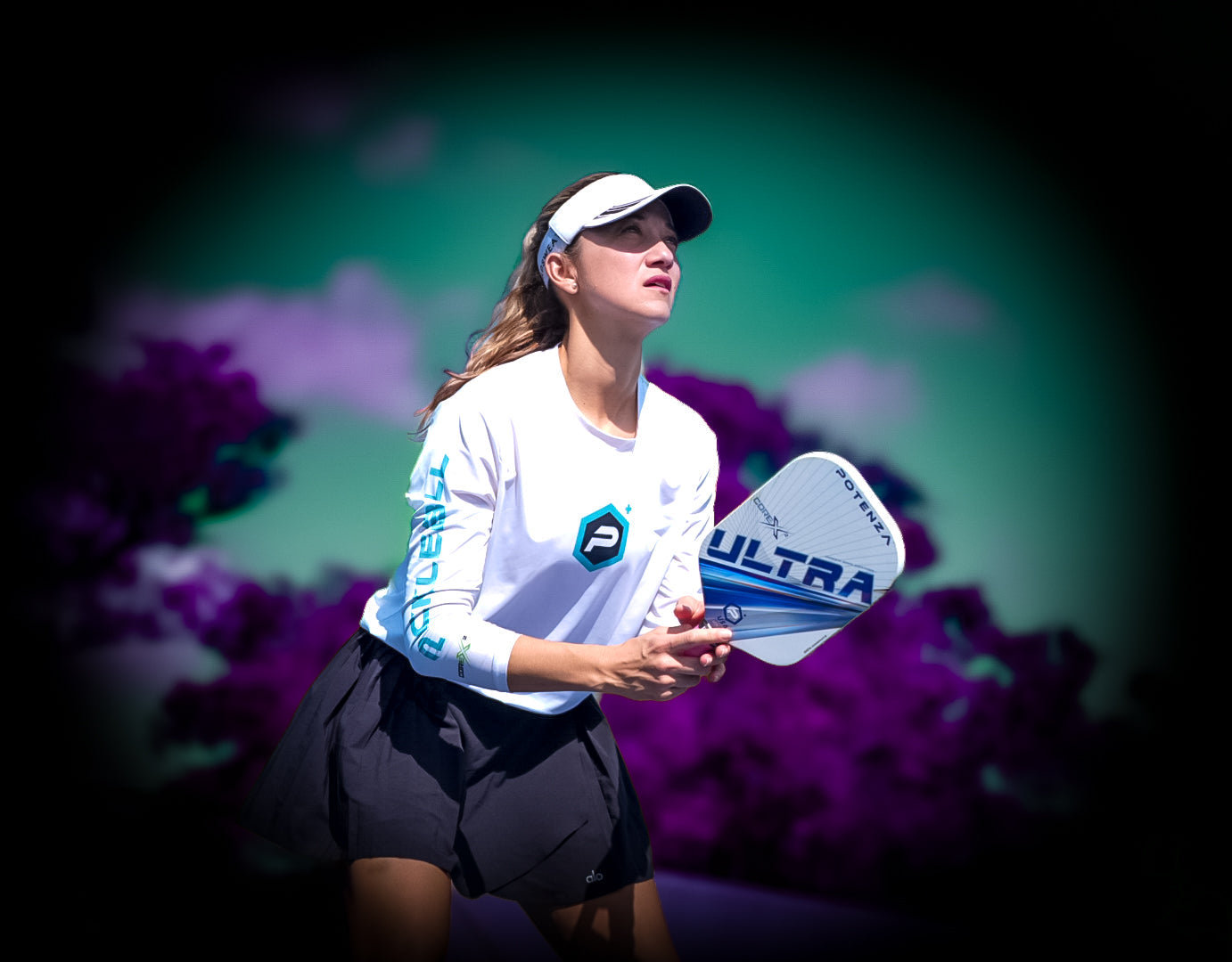 A female pickleball player in a visor, white long-sleeve shirt, and black skirt holds a Potenza Pickleball ULTRA+ COREx2 graphite paddle, looking upward with focus against a blurred background of purple foliage and a glowing halo effect.