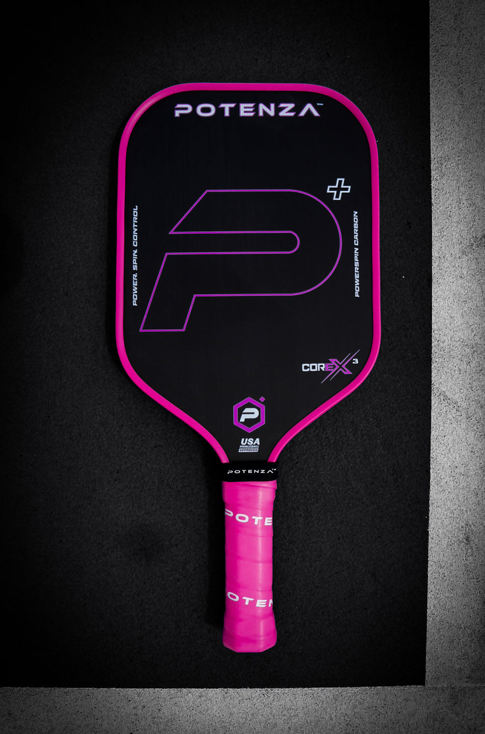 The Potenza Pickleball P+ PowerSpin Carbon COREx3 (Neon Pink) features a black carbon fiber face, neon pink edges and grip, and bold branding details, including a large stylized "P", all set against a dark textured background.