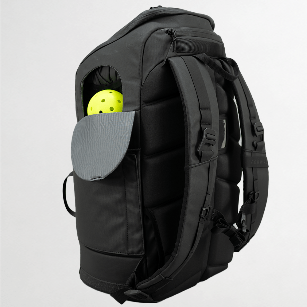 The FORWRD Court Caddy Pickleball Bag stands upright with padded straps and a back panel. An open side pocket displays two yellow pickleballs. The gray pocket flap shows a zigzag pattern, all set against a light gray background.
