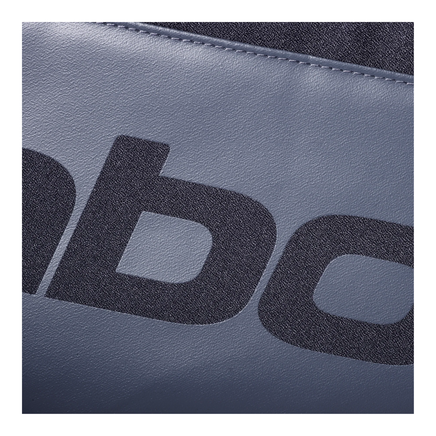 A close-up of textured blue-gray recycled synthetic fabric from the Babolat COURT S Padel Bag by Padel USA shows bold black letters and visible stitching near the top edge.